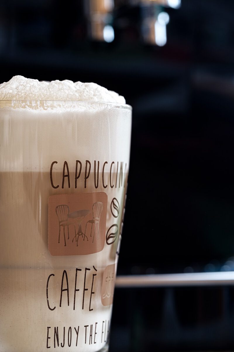 Close-up of latte macchiato with foam art in a transparent glass, placed on a saucer with a spoon, on a wooden table.